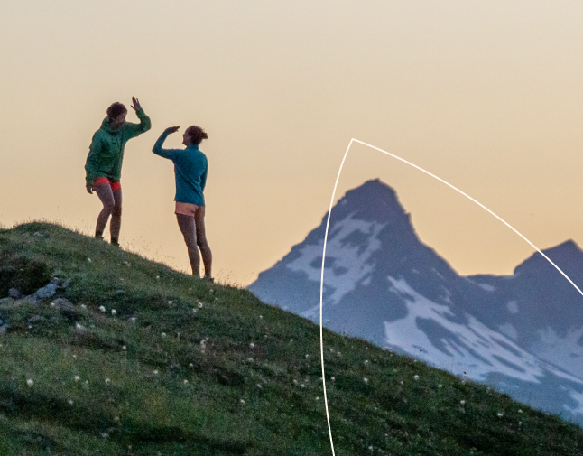 Deux collègues assis sur un canapé dans un bureau moderne et lumineux, souriant et regardant ensemble un ordinateur portable. L’une des personnes montre l’écran du doigt tandis que l’autre se penche avec attention, avec des étagères de plantes en arrière-plan.