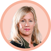 Portrait professionnel d’une femme blonde souriante, en veste de costume foncée, sur un fond circulaire beige