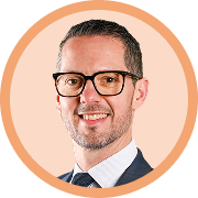 Portrait professionnel d’un homme portant des lunettes, costume sombre et cravate, souriant sur un fond circulaire beige