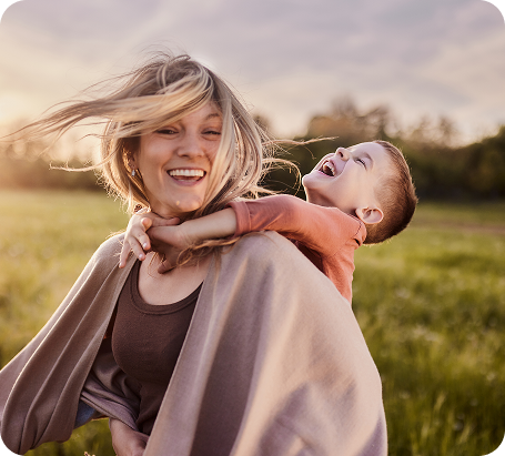 Une jeune femme portant dans son dos un enfant qui rigole.